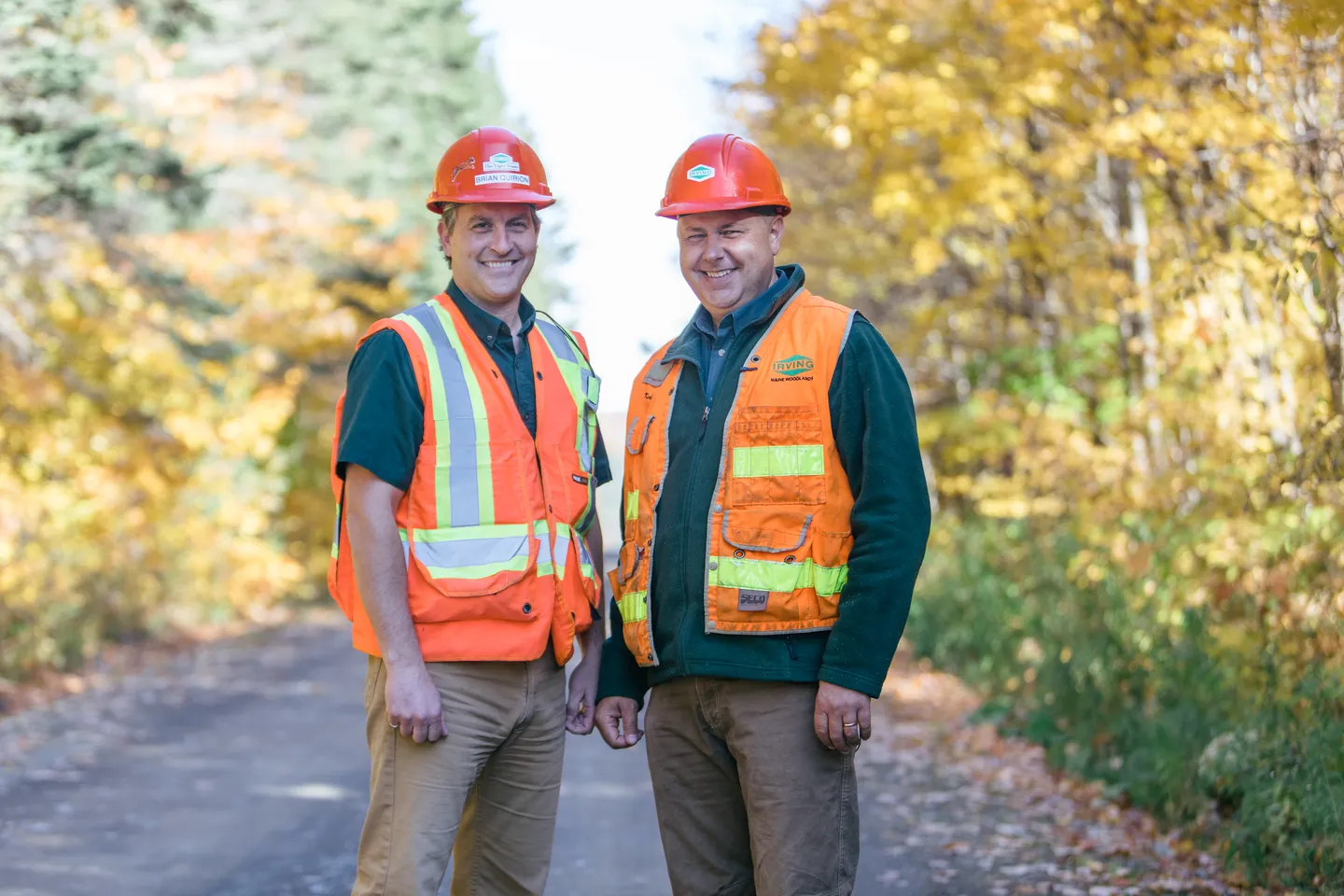 Two Irving Woodlands foresters smiling at camera, surrounded by trees.